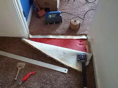 Carpet and pad pulled back with an air mover drying the floor after a leak below